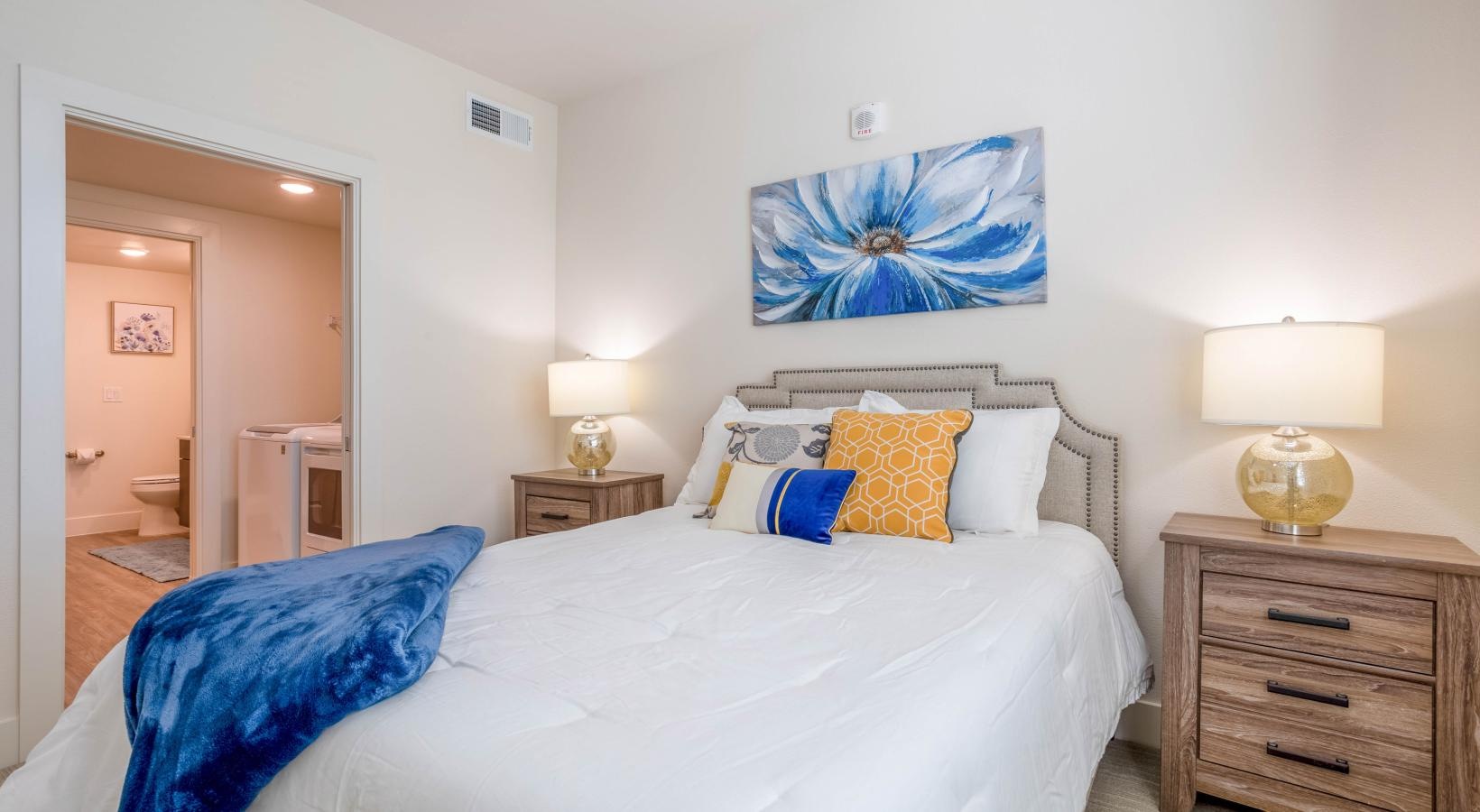 Relax and recharge in beautiful and spacious bedrooms Model bedroom at our senior living apartments in Pearland, Texas, featuring white bedspread and a view of the laundry closet.